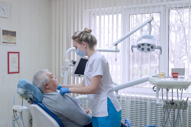 Zahnarzthelferin in Schutzmaske mit älterem Patienten vor der Untersuchung in der Zahnklinik