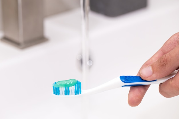 Zahnbürste mit Zahnpasta in der Hand des Mannes auf dem Hintergrund des Waschbeckens.