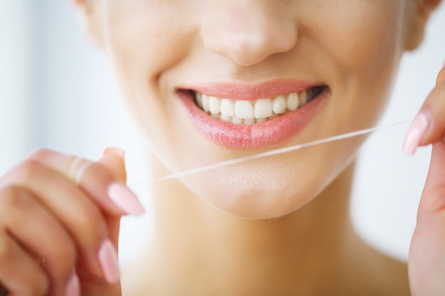 Zahnpflege, schöne lächelnde Frau, die gesunde weiße Zähne flossing ist