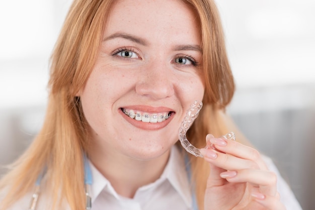 ZahnpflegeLächelndes Mädchen mit Zahnspangen hält Aligner in den Händen und zeigt den Unterschied zwischen ihnen