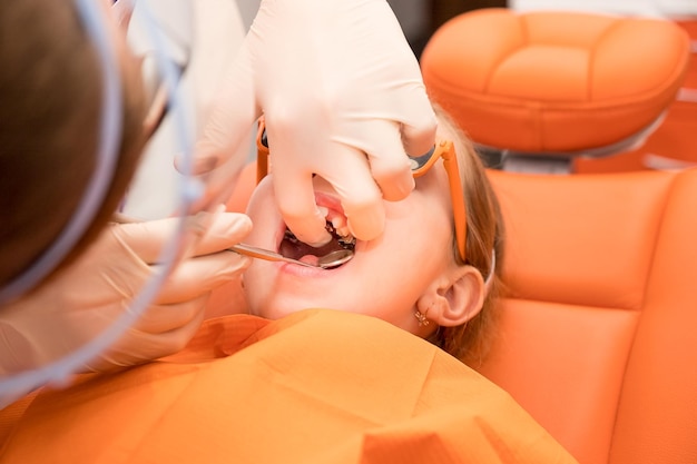 Zahnplatte Erweiterung des Kiefers bei einem Teenager-Mädchen, das eine kieferorthopädische Platte in ihren Händen hält. Der kieferorthopädische Arzt untersucht Zähne und Zahnfleisch des kleinen Mädchens