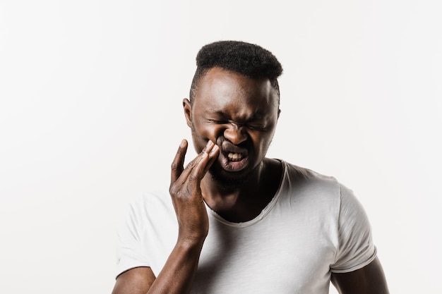 Zahnschmerzen des afrikanischen Mannes auf weißem Hintergrund Afroamerikaner berühren Wange und fühlen sich verletzte Zähne auf weißem Hintergrund Kariesinfektion oder Verletzung des Zahns oder des Zahnfleischs