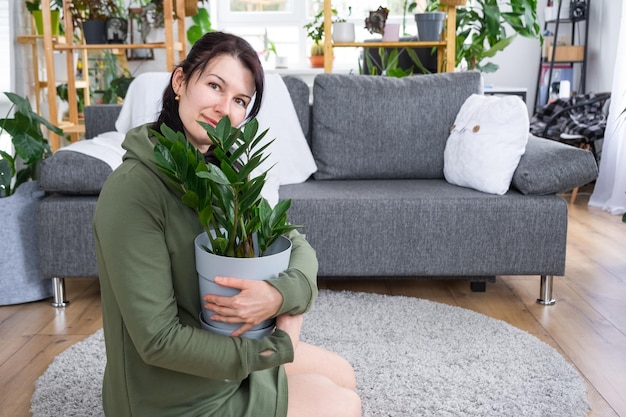 Zamioculcas despretensiosas e populares nas mãos de uma mulher no interior de uma casa verde com coleções de plantas domésticas