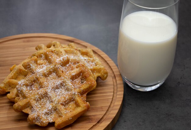 La zanahoria se enrolla con el azúcar en polvo en un tablero de madera con un vaso de leche.