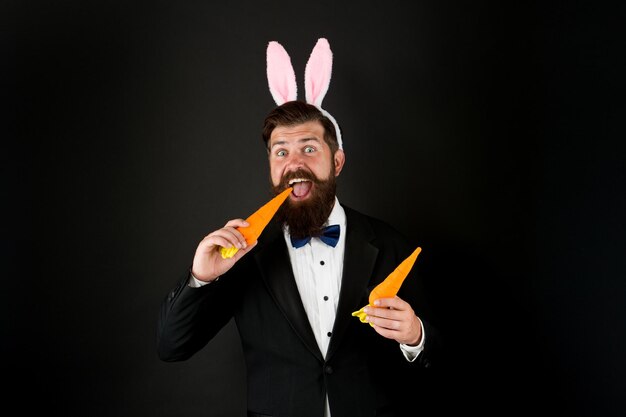 La zanahoria es buena para los dientes. Celebración de las vacaciones de Pascua. Día de Pascua. Anfitrión del evento. Celebrar Pascua. Hombre con barba y orejas largas. Hombre de negocios con orejas largas. Accesorio de traje de conejito de desgaste de hombre guapo.