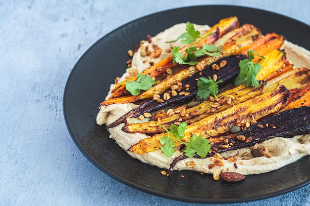 Foto zanahorias al horno multicolores con hummus en plato negro receta vegana