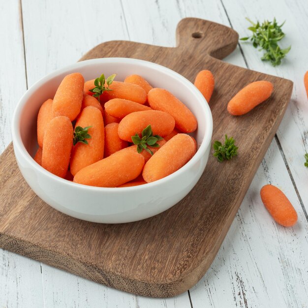 Zanahorias baby en un bol sobre una mesa de madera con hierbas