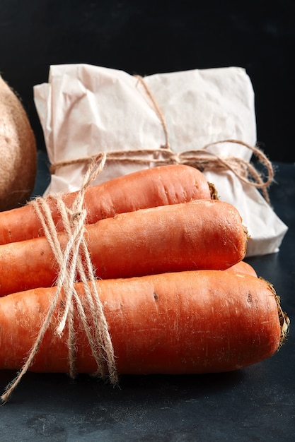 Zanahorias frescas, fondo oscuro. Concepto de entrega de alimentos, envases ecológicos. Copie el espacio, primer plano.