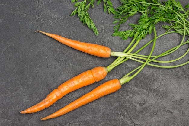 Zanahorias frescas con tapas verdes en la mesa. Fondo negro. Endecha plana