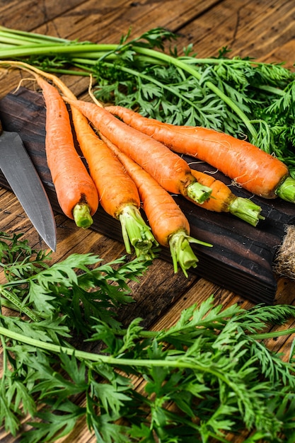 Zanahorias naranjas con hojas sobre una tabla para cortar.