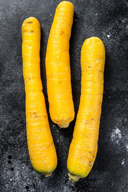 Zanahorias orgánicas amarillas crudas frescas. Superficie negra. Vista superior