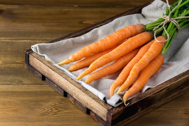 Zanahorias orgánicas frescas con tapas verdes sobre fondo de madera Cosecha de zanahoria madura Caja de madera horizontal