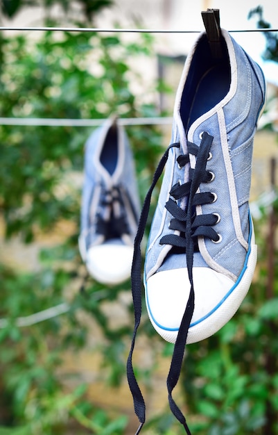 Foto zapatilla azul vieja colgando de una cuerda detrás de una pinza de madera