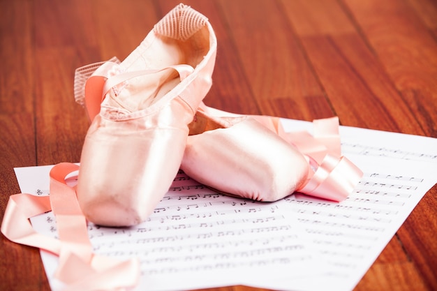 Zapatilla de ballet sobre un piso de madera sobre una partitura musical.