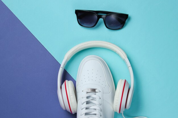 Zapatillas con auriculares y gafas de sol sobre fondo de color