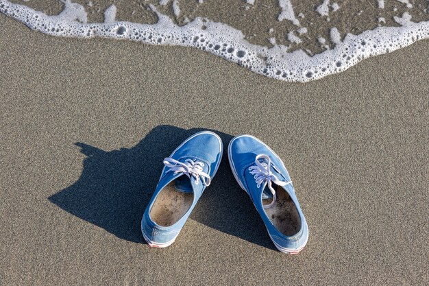 zapatillas azules que proyectan una sombra se encuentran en la playa con una ola que se avecina