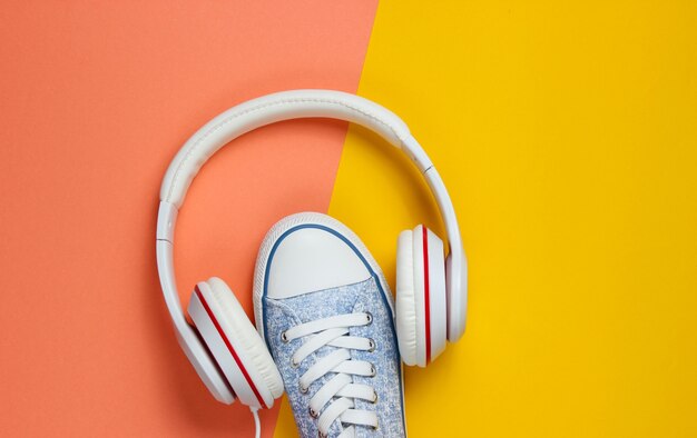 Zapatillas blancas con auriculares sobre fondo de color. Concepto de música. Endecha plana, mínima.