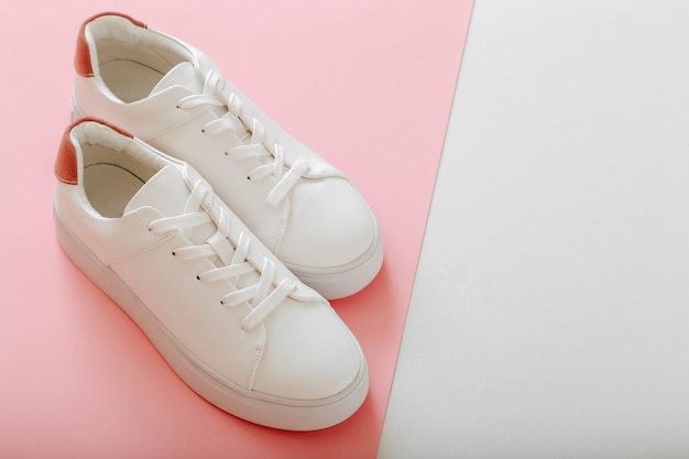 Zapatillas blancas sobre fondo de color rosa. Zapatos femeninos de cuero blanco con cordones sobre fondo rosa con espacio de copia. Par de zapatillas de deporte con estilo Calzado de mujer cómoda ropa deportiva hipster.