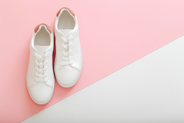 Zapatillas blancas, zapatos femeninos de cuero blanco con cordones sobre fondo rosa. Par de zapatillas de deporte con estilo Calzado de mujer cómoda ropa deportiva hipster. Espacio de copia de vista superior.