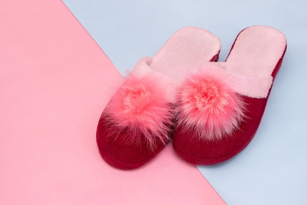 Zapatillas de casa de mujer rosa y burdeos suaves con pompones sobre un fondo rosa y azul cálido