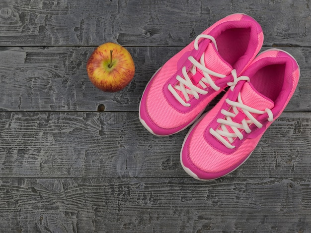 Zapatillas de color rosa para las clases de gimnasia en el gimnasio y una manzana madura en un piso de madera.