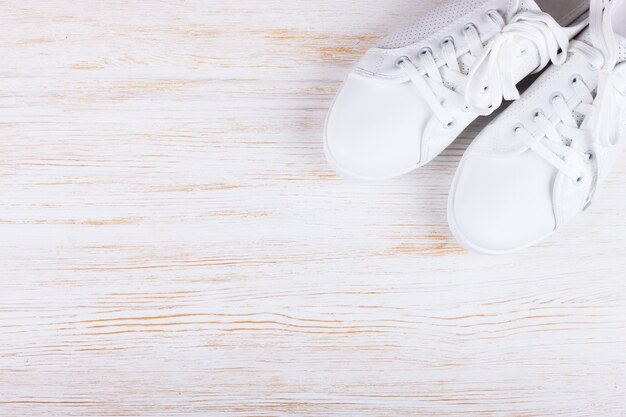 Zapatillas de deporte femeninas blancas sobre fondo blanco de madera con espacio de copia. vista superior, endecha plana.