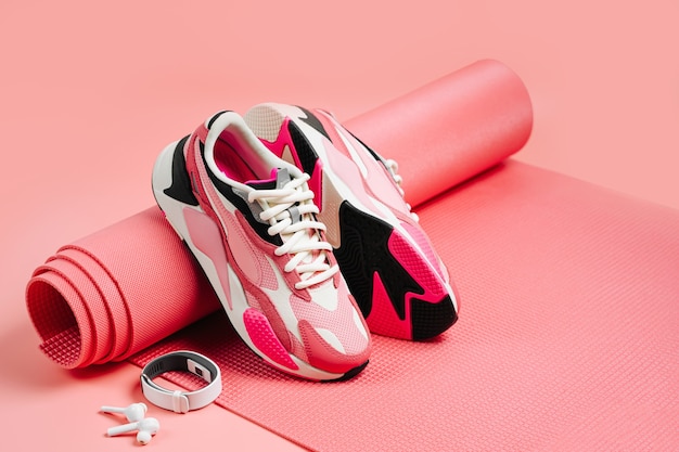 Zapatillas de deporte de moda brillante con pulsera de fitness y esterilla de yoga rosa. Estilo de vida saludable.