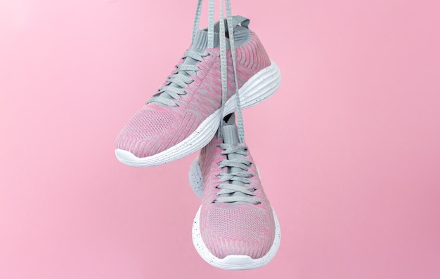 Zapatillas deportivas femeninas para correr o fitness colgando sobre fondo rosa