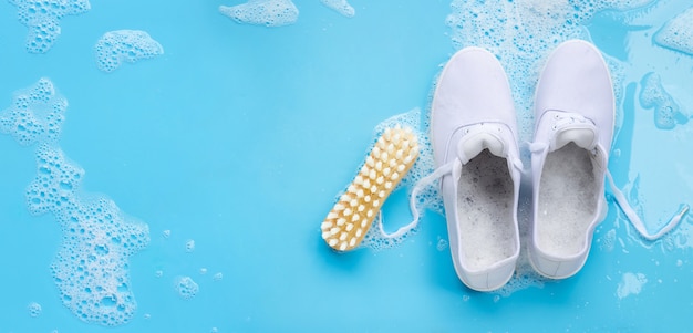 Zapatillas con espuma de detergente en polvo de disolución en agua y cepillo de madera. Lavado de zapatos sucios.