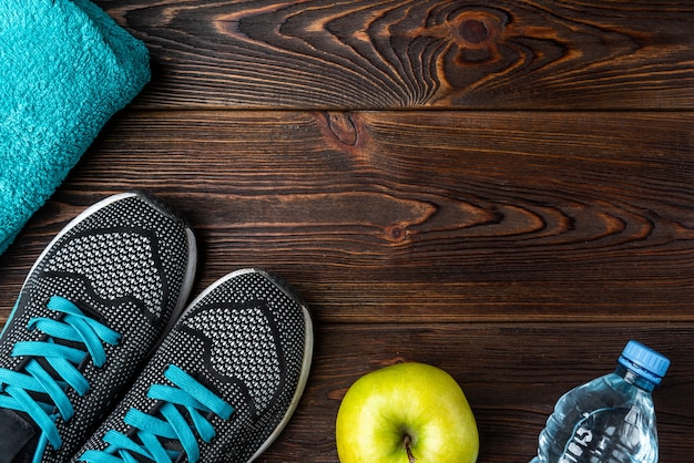 Zapatillas de fitness, toalla y manzana en madera oscura.