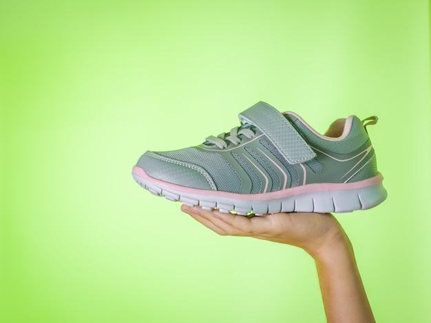Zapatillas grises de moda en la mano de un niño sobre un fondo verde. Zapatos deportivos. Tendencia del color.
