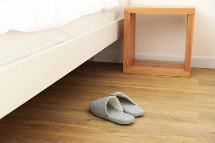 Zapatillas grises en el suelo junto a la cama.