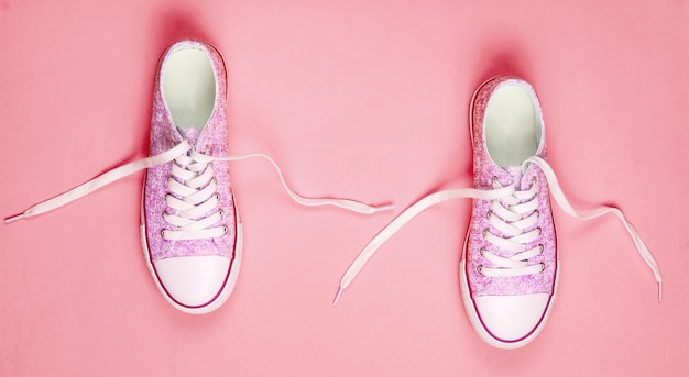 Foto zapatillas de moda con cordones desatados sobre fondo rosa