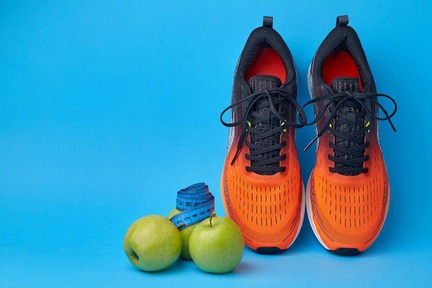 Zapatillas naranjas cinta métrica y manzanas de frutas sobre un fondo azul.