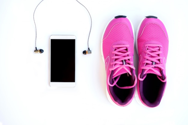 Zapatillas rosa para mujer, teléfono y auriculares sobre un fondo blanco.