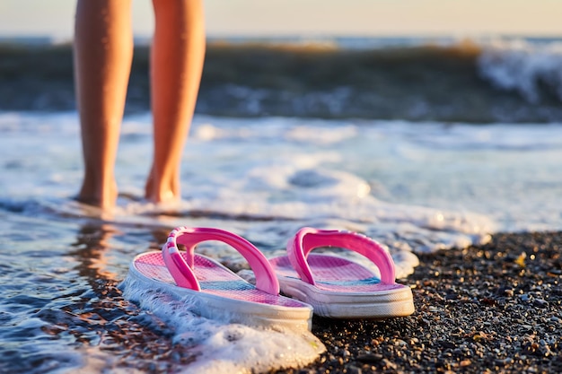 Zapatillas rosas para niños en una playa de guijarros con piernas de niña en el fondo