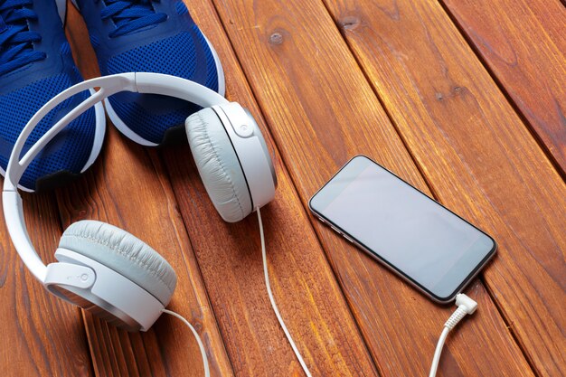 Zapatillas y teléfono móvil con auriculares en mesa de madera