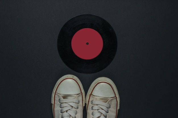 Zapatillas viejas retro y disco de vinilo sobre un fondo negro. Años 80. Vista superior