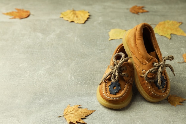 Zapatos de bebé y hojas sobre fondo gris con textura.