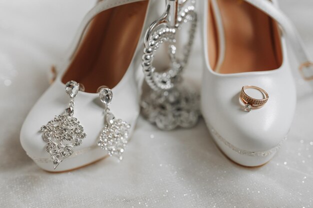 Zapatos de boda de la novia con pendientes y un anillo de bodas de oro en el tren del vestido de novia