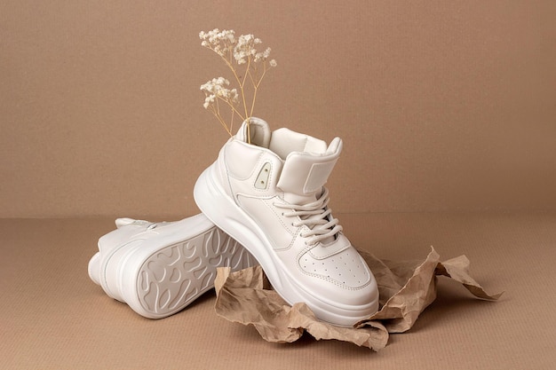 Foto zapatos de cuero ecológico un par de zapatillas beige con flores secas sobre fondo marrón concepto de estilo de vida deportivo informal