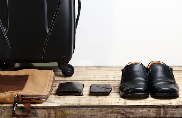 Zapatos de cuero negro, billetera, teléfono inteligente móvil y bolsa de viaje para equipaje en la mesa de madera