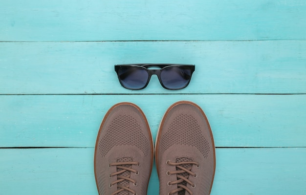 Zapatos de hombre y gafas de sol sobre fondo de madera azul. Vista superior