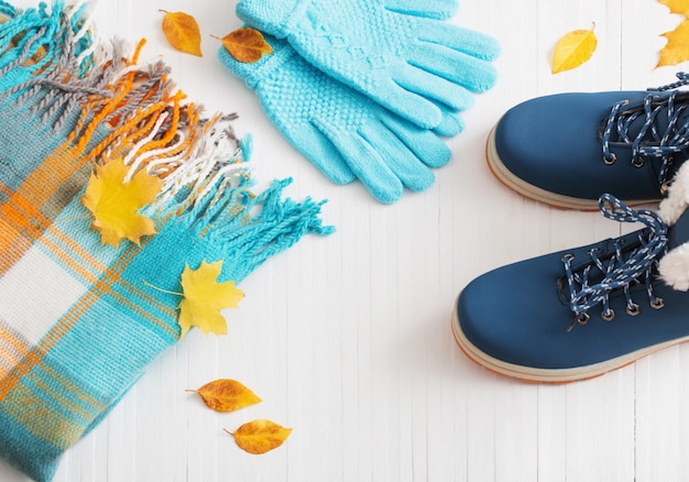 Zapatos de invierno azul y guantes sobre fondo blanco de madera