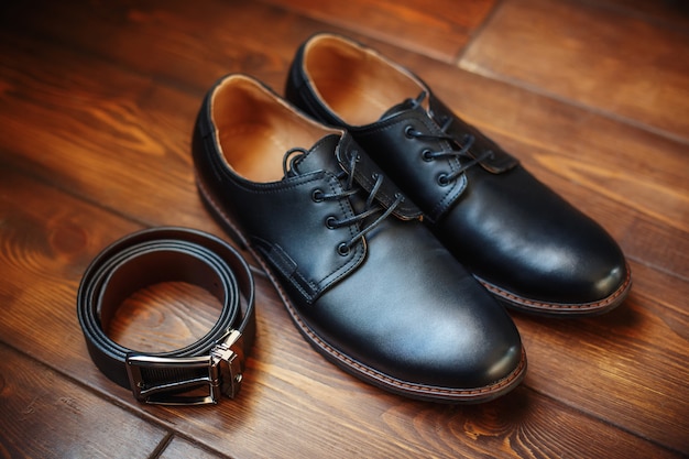 Zapatos masculinos de cuero negro y cinturón sobre superficie de madera