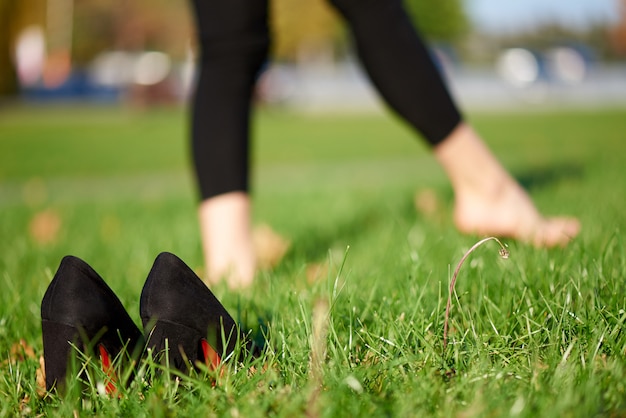 Zapatos negros en la hierba sobre un fondo de piernas femeninas descalzas.