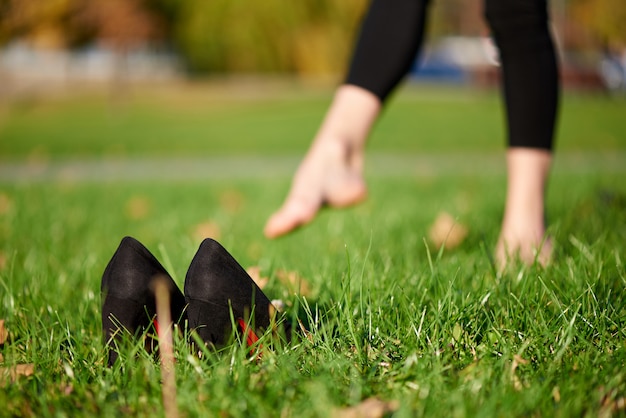 Zapatos negros en la hierba sobre un fondo de piernas femeninas descalzas.