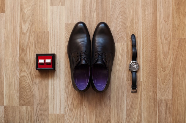 Zapatos negros, reloj y gemelos en el piso. Accesorios para el novio el día de la boda.