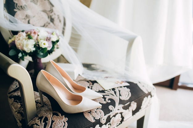 Zapatos de novia con un ramo de rosas y otras flores en el sillón tha