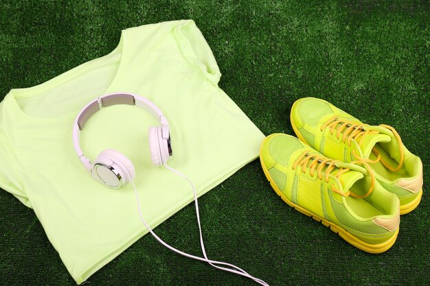 Zapatos de ropa deportiva y auriculares sobre fondo de hierba verde